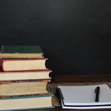 A pile of books sat next to a pad of paper and a pen
