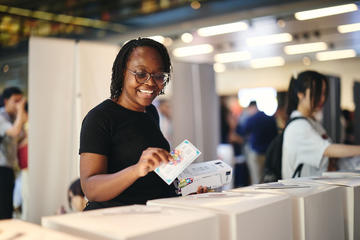 A person smiling posting a fake #StartedinOxford Showcase 2025 cash note into a voting box