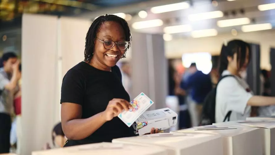 A person smiling posting a fake #StartedinOxford Showcase 2025 cash note into a voting box
