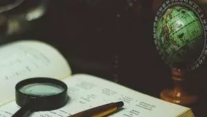 An open book sat next to a mini globe with a magnifying glass and pen