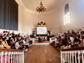 two speakers sat in front of a audience giving a talk