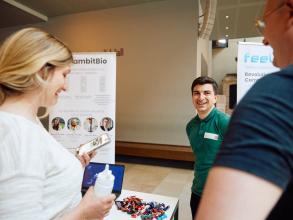 A GambitBio founder standing next to his stand chatting to Demo Night event attendees