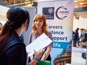 The Careers Services, University of Oxford team member stood next to their stand and chatting to Demo Night attendee