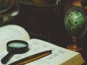 An open book sat next to a mini globe with a magnifying glass and pen